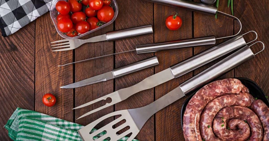 Barbecue tools and sausage on wooden table